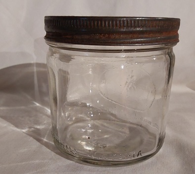 A squat round clear glass jar with a metal screw on lid.