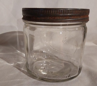 A squat round clear glass jar with a metal screw on lid.