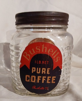 A medium sized squat clear glass Bushells Coffee jar, with a tin screw on lid.