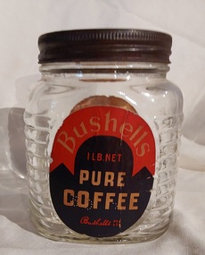 A medium sized squat clear glass Bushells Coffee jar, with a tin screw on lid.