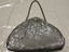 Front of small silver purse, half moon shaped with small chain handle. Ruched at top to a small frame opening closed by a square metal clasp. Made of silver mesh chain mail.