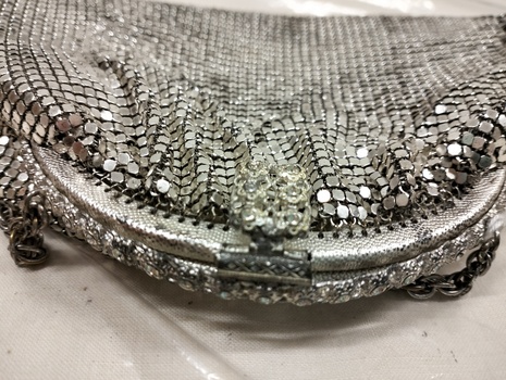 Closeup photo of purse’s semi circle frame opening, clasp with metal detailing and back of the frame lined with diamantés 
