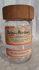 A clear glass jar for English Marmalade with a cracked brown wooden screw-top lid. 