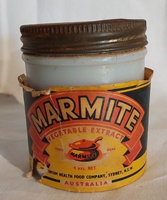 A small white glass Marmite jar with a rusted screw top metal lid and a loose paper label.