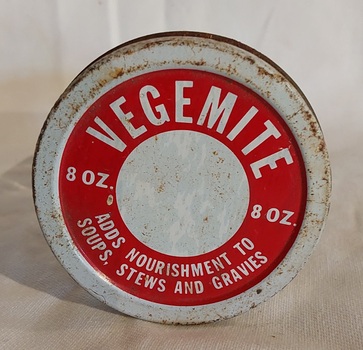 A small clear glass Vegemite jar with a rusted white and red screw top metal lid. 