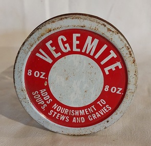 A small clear glass Vegemite jar with a rusted white and red screw top metal lid. 