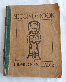 A very damaged brown softcover book with the title, Second Book of the Victorian Readers printed in black lettering on the front cover.