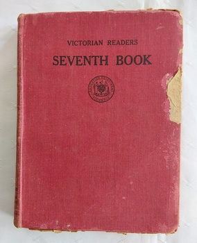 A damaged red cloth covered hardcover book with the title Victorian Reader Seventh Book, printed in black lettering at the top of the front cover.