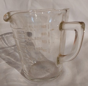 A small clear vintage glass measuring jug for cooking with two pouring lips and a handle.