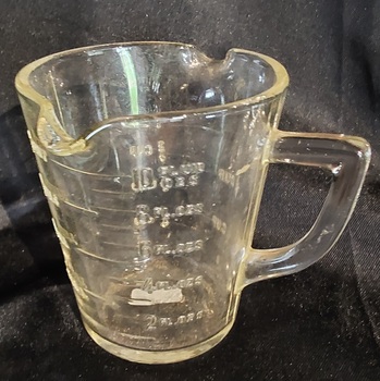 A small clear vintage glass measuring jug for cooking with two pouring lips and a handle. 