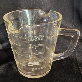 A small clear vintage glass measuring jug for cooking with two pouring lips and a handle. 