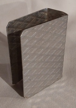 An open aluminium matchbox holder, with a diagonal pattern inside and out.