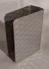 An open aluminium matchbox holder, with a diagonal pattern inside and out.