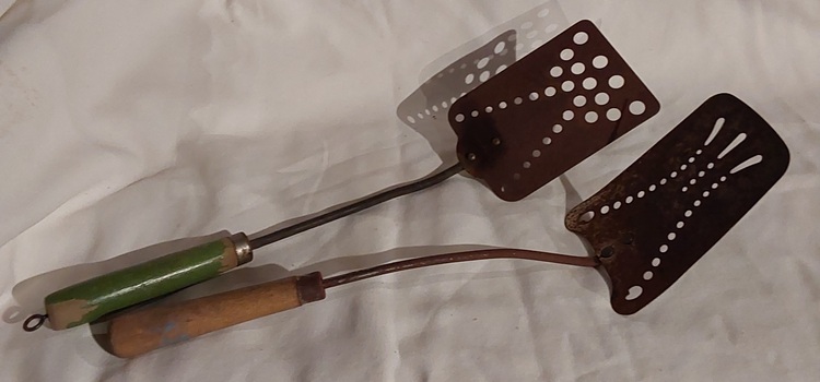 Two egg slides or spatulas with varying sized holes on the slide and wooden handles.