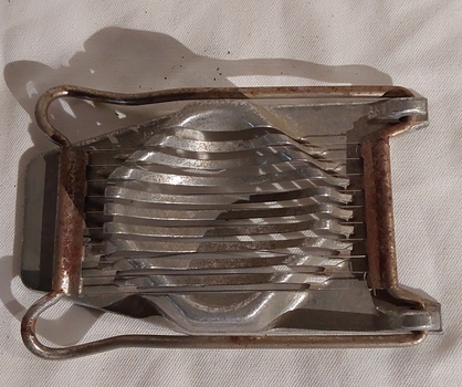 A stainless steel egg slicer with a base which has a raised stand or support with slats to hold the cooked, shelled egg.