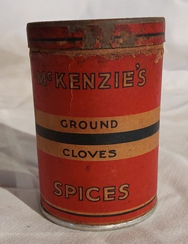 A small vintage cardboard cylindrical container of McKenzie's Ground Cloves with a red and navy striped printed paper label with white print.