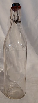 A large clear glass Fowlers Fruit Juice bottle with a wire clip and black stopper with a red rubber seal. 
