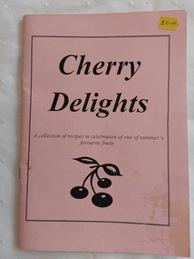 A small pink covered Cherry Delights recipe book with the title printed in black and a few cherries drawn below.