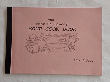 A small rectangular pink covered home made Soup Cook Book with the title and an illustration of a bowl of soup with vegetables around it.