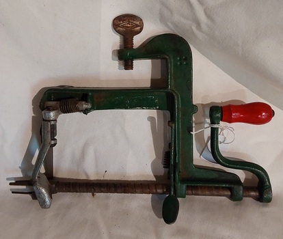 A vintage green steel apple peeler made from cast iron with a red wooden knob on the turning handle. 