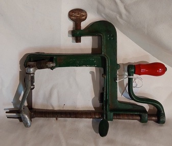 A vintage green steel apple peeler made from cast iron with a red wooden knob on the turning handle. 
