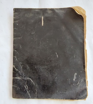 A black covered school exercise book with arithmetic, spelling, grammar handwritten in black ink.