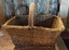 A large heavy cane basket with a strong curved cane covered handle which is attached to the basket with leather straps.