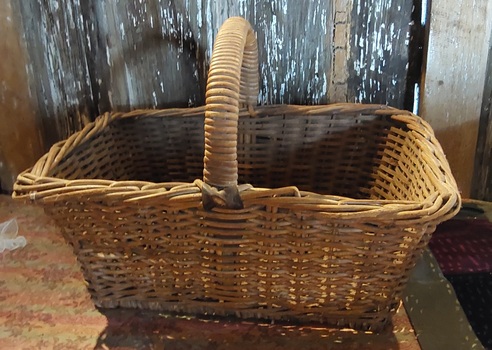 A large heavy cane basket with a strong curved cane covered handle which is attached to the basket with leather straps.
