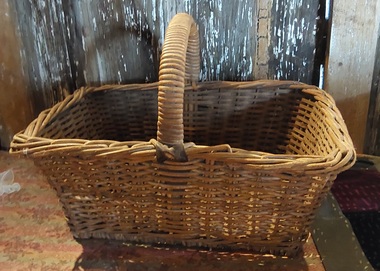 A large heavy cane basket with a strong curved cane covered handle which is attached to the basket with leather straps.
