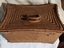 A large lidded firm natural coloured raffia woven basket with two bound plastic woven cane type hinged handles on the lid attached by two pieces of plastic for portability. 