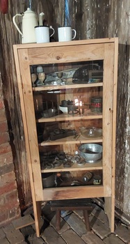 A tall rough finished homemade pine cabinet with five internal shelves and a lockable glass fronted door. 