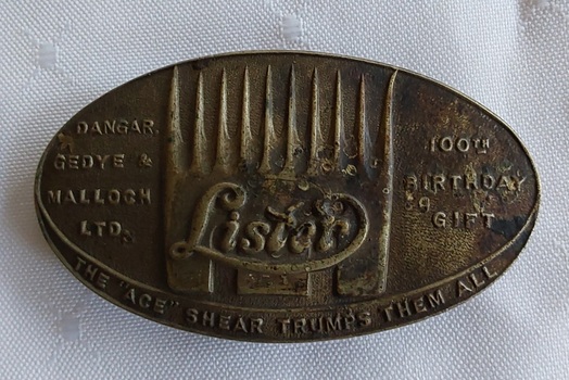 An oval shaped brass and metal Lister belt buckle with the name, a symbol of shears and the manufacturing details on the front.