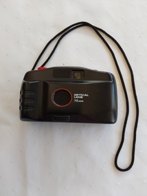 A black plastic lightweight no brand 35mm Optical Lens automatic focus camera with a black woven cotton neck cord attached with a bslck vinylcase.