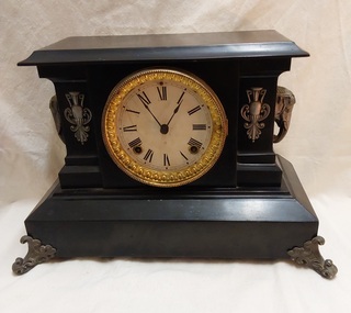 A black vintage Ansonia cast iron Mantel Circus clock with a glossy finish and a brass elephant head on each side.