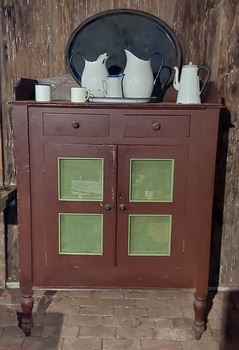 A vintage brown painted wooden meat safe with two drawers at the top with round brown knobs.There are two doors with ventilation panels below.