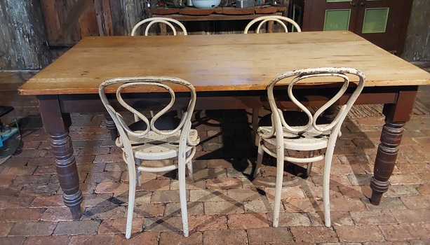 A vintage very worn and marked light brown rectangular wooden kitchen table with four painted dark brown thick turned legs.
