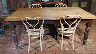 A vintage very worn and marked light brown rectangular wooden kitchen table with four painted dark brown thick turned legs.
