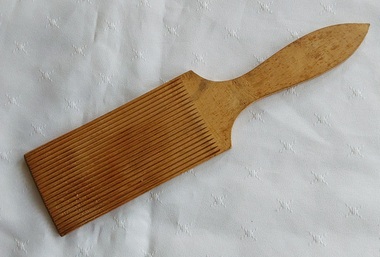 A vintage handmade light coloured wooden butter pat made from one piece of wood with one smooth side and the other ridged.