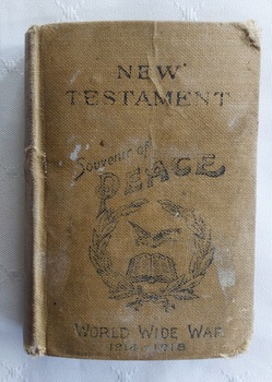 A miniature light tan cloth covered New Testament with a black circular laurel wreath, a book and dove stamped on the front cover.