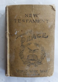A miniature light tan cloth covered New Testament with a black circular laurel wreath, a book and dove stamped on the front cover.