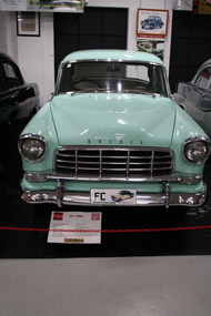 Holden FC model 4 door sedan. Two toned green finish on outer with the darker shade on the roof and rear side panels. Wire scrrwen stone guard covers on both headlamps. Chrome grille with over riders.