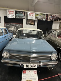 Blue four door sedan, with white roof. Again broad grille with headlights incorporated Chrome bumper. Holden name plate over the top of the grille