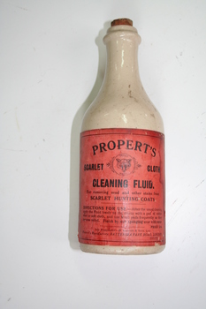 Beige long neck ceramic bottle with red label stating that the bottle contains "Properts Scarlet Cloth Cleaning Fluid"
