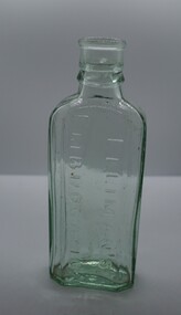 Clear glass bottle with contents and maker moulded in the front