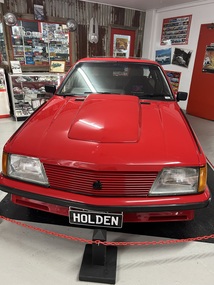 Red bodied four door sedan with sunroof, bonnet scoop, deflectors on both quarter panels, air deflector mounted on boot