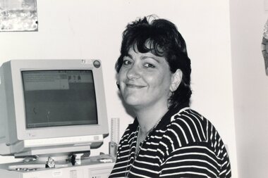 Photograph, Lady smiling in front of a computer at the Community House  (POCH)