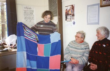 Photograph, One lady showing others a quilt at Park Orchards Community House
