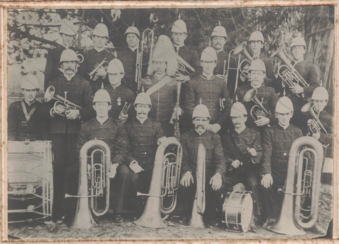 Black and white photograph of a group of men in uniform and helmets with brass instruments and drums.