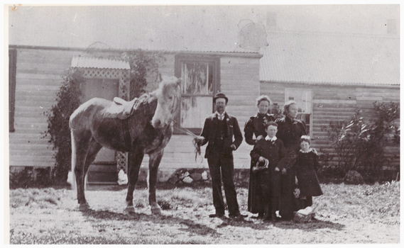 Man holding a horse outside a house.