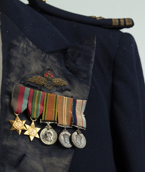 Small medal set with two gold stars and three round silver medals on striped ribbons, fastened to navy blue jacket lapel.  Embroided RAF badge sewn just above medals
